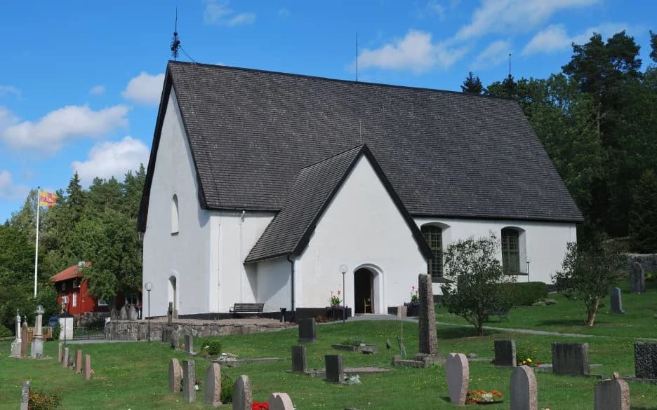 Vätö kyrkas vita fasad, mörka tak och kyrkogård under blå himmel